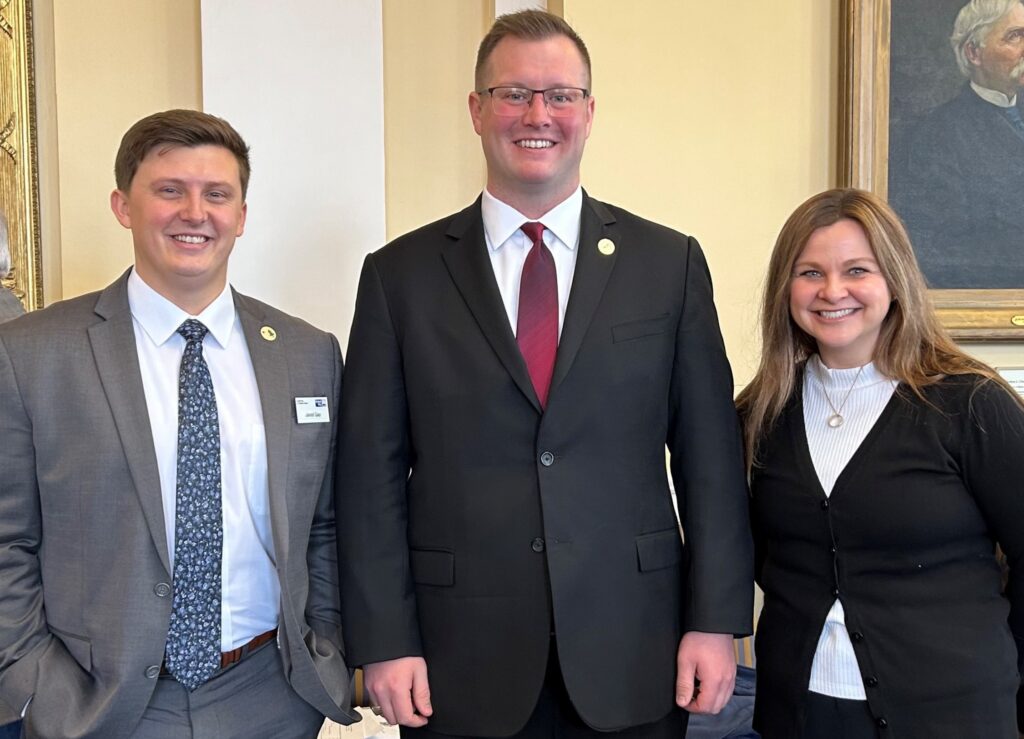 Jared Gay, Director of Public Policy and Advocacy for United Way of Southern Maine, Senator Trey Stewart (Aroostook), and Nikki Williams, 211 Maine Program Director, pose after the resolution passed in the State Senate.